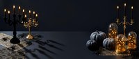 Dark elegant Halloween scene with black pumpkins, vintage candelabras, glowing lights and gothic decorations on textured surface for autumn celebrations.