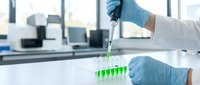 Laboratory scientist in protective gloves using pipette to transfer green liquid samples into test tubes for medical research and chemical analysis in modern lab.