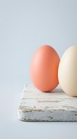 Two colorful Easter eggs in coral and cream tones sitting on rustic white wooden surface against neutral gray background for spring holiday decorations.