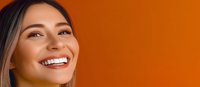 Young Asian woman with bright white smile and natural makeup looking up against vibrant orange background, expressing joy and confidence in dental care concept.