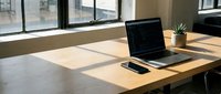 Laptop and smartphone on wooden desk by bright window in modern office space with natural sunlight for workspace and business design projects.