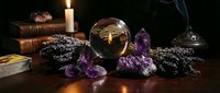 Mystical fortune telling setup with crystal ball, amethyst crystals, burning candle, ancient books and tarot cards on wooden table for spiritual guidance.