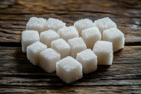 White sugar cubes arranged in heart shape on rustic wooden table background, macro close up view with selective focus and crystalline texture.