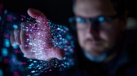 Caucasian male tech professional interacting with glowing digital hologram particles in dark room with blue technology visualization effects.