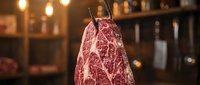 Whole cured meat ham hanging with twine in warm restaurant kitchen with blurred background and hanging lights for food service.