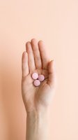 Open hand holding three pink pills or capsules against neutral beige background, suitable for healthcare, medicine, pharmacy, and wellness design projects.