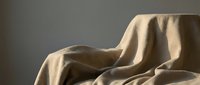 Soft beige linen fabric draped elegantly with natural folds and shadows creating minimalist textile composition for home decor and fashion design projects.