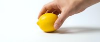 Hand holding a fresh ripe yellow lemon on white background, showcasing vibrant citrus fruit for food, health, and nutrition concepts.