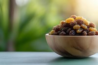 Fresh and dried golden raisins in wooden bowl on blue table against blurred green garden background, healthy natural snack for cooking and eating.