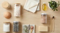 Spa and wellness products arranged on wooden surface with salt, oils, soap, towels, brushes and potted plant for beauty and skincare routines.