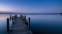 Wooden pier extending into calm lake at twilight with serene purple and blue sky reflecting on still water, suitable for travel and nature backgrounds.