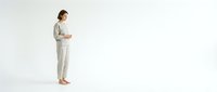 Pregnant woman in beige casual outfit standing on white background, expecting mother in comfortable clothing for maternity lifestyle content.