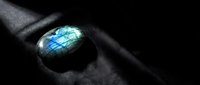 Polished labradorite gemstone with brilliant blue-green flash displaying natural iridescence on dark textured surface for jewelry and mineral collection.