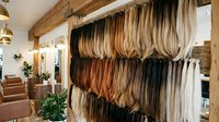 Hair extension display wall in professional salon showing various blonde brown and black color samples organized on wooden shelves for styling consultation.