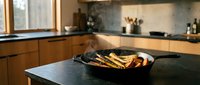 Grilled zucchini slices in cast iron skillet on black kitchen counter with wooden cabinetry and window light for cooking and food preparation.