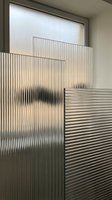Modern corrugated metal panels with ribbed texture create industrial aesthetic in contemporary interior space with natural light filtering through translucent barriers.