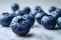 Fresh ripe blueberries with water drops on marble background, macro shot showing texture and natural organic appearance in cool blue tones.