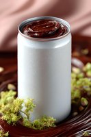 Creamy chocolate mousse served in white aluminum can with water drops, garnished with fresh green moss on dark wooden surface against pink background.