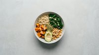 Healthy Buddha bowl with quinoa, chickpeas, roasted sweet potato, fresh spinach and avocado on neutral background for wellness nutrition content.