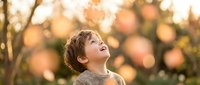 Young Caucasian boy with curly hair looking up with wonder and joy in golden autumn sunlight with warm bokeh background outdoors.