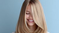 Young woman with healthy straight blonde hair smiling against blue background, showcasing natural beauty and haircare results for beauty and wellness advertising.