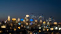 Soap bubbles floating against blurred city lights at dusk creating magical bokeh effect with urban skyline background for dreamy atmospheric concepts.