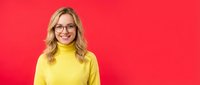 Young blonde Caucasian woman wearing glasses and yellow turtleneck sweater smiling cheerfully against bright red background for lifestyle marketing.