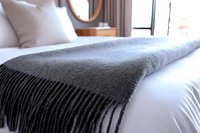 Cozy gray wool blanket with fringe draped over white bedding in modern bedroom interior, creating warm and inviting atmosphere for hospitality and home decor.