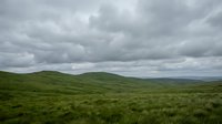 Lush rolling green hills under dramatic cloudy sky, expansive grassland landscape for nature, travel, and environmental design projects.