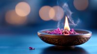 Decorative brass oil lamp with pink petals and burning flame against blurred bokeh background creates serene spiritual ambiance on blue surface.
