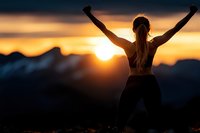 Young woman celebrating success with raised arms at mountain summit during golden sunrise, silhouette against dramatic sky for motivation and achievement concepts.