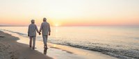 Senior couple walking hand in hand on beach at sunset, romantic golden hour moment by ocean waves, peaceful retirement lifestyle and love.