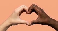 Two diverse hands forming heart shape symbol representing love unity and togetherness against warm peach background for romantic greeting cards.