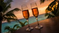 Two champagne flutes filled with golden sparkling wine on wooden surface with tropical palm trees and sunset ocean view creating romantic atmosphere.