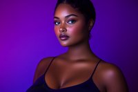 Young African American woman with glowing skin and dramatic makeup against purple background, professional beauty portrait highlighting natural features and glossy lips.