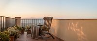 Wooden rocking chairs on a rooftop terrace at sunset with potted plants and ocean view, perfect for relaxation and outdoor design projects.