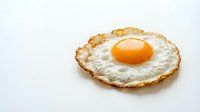 Crispy fried egg with golden yolk and lacy edges isolated on white background for breakfast menu design and culinary projects.