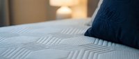 Cozy bedroom scene with navy blue decorative pillow resting on white textured bedding, soft warm lighting in background, perfect for home decor and lifestyle content.