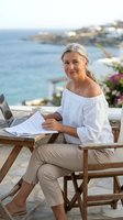 Mature blonde woman working remotely on laptop at seaside terrace with ocean view, digital nomad lifestyle and flexible work arrangements.