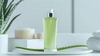 Green cosmetic bottle with aloe vera leaf on white ceramic plate, minimalist spa composition against light background for beauty and skincare advertising.