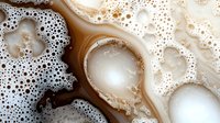 Coffee foam with bubbles and cream swirls creating abstract patterns on brown liquid surface for beverage and cafe concepts.