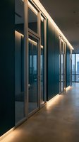 Modern office corridor with glass partitions and warm LED lighting creating professional workspace atmosphere for corporate interior design.