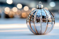 Elegant silver Christmas ornament with metallic stripes on white surface with warm bokeh lights background for holiday decorations and festive celebrations.
