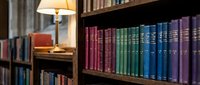 Cozy library interior with colorful book collection on wooden shelves and warm lamp lighting creating peaceful reading atmosphere for study and research.