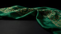 Luxurious emerald green silk scarf with ornate golden paisley pattern draped elegantly on dark surface for fashion and textile design projects.