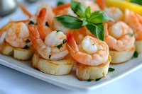 Grilled shrimp appetizers served on toasted baguette rounds with fresh herbs and lemon garnish, arranged on white plate for catering and party events.