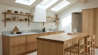 Bright Scandinavian kitchen with oak cabinets, granite countertops, skylights, open shelves, and a wooden island with wicker chairs.
