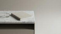 Marble tabletop with glass of water, closed notebook and pen arranged on minimalist workspace for office, study or creative projects.