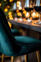 Elegant emerald velvet bar stool with gold legs against blurred bokeh lights and wine glass, creating luxurious restaurant atmosphere for hospitality industry.