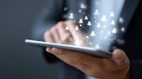 Glowing social network icons emerging from digital tablet screen held by business professional in dark setting, representing digital connectivity.